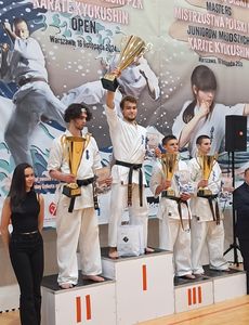 Zawodnicy karate w strojach sportowych stojący na podium i trzymający puchary w swoich rękach.