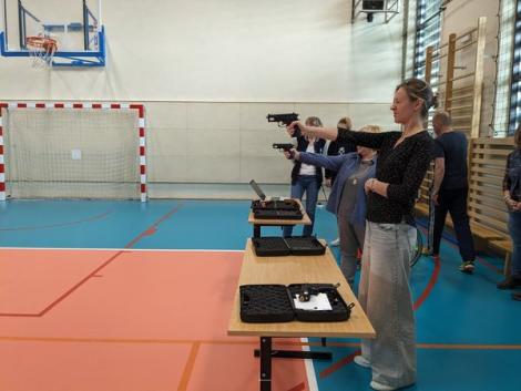 Photo no. 2 (6)
                                                         Zdjęcie, hala sportowa, przy stolikach stoją uczestnicy spotkania, dwie kobiety strzelają do celu z pistoletu laserowego
                            